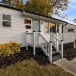 Exterior of a white mobile home with a small wooden porch and stone-look skirting.